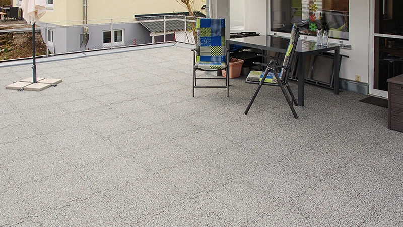 En una azotea se han colocado baldosas de terraza WARCO en tono gris veteado, fabricadas con granulado de caucho aglutinado con PU. Su encaje tipo puzzle garantiza un ajuste preciso y combina resistencia a la intemperie con larga durabilidad. El material estable en su forma amortigua el ruido de pisadas y aporta un aspecto ordenado y pulcro. Además, ofrece superficie antideslizante y gran comodidad al andar, haciéndolo muy práctico para su uso diario.