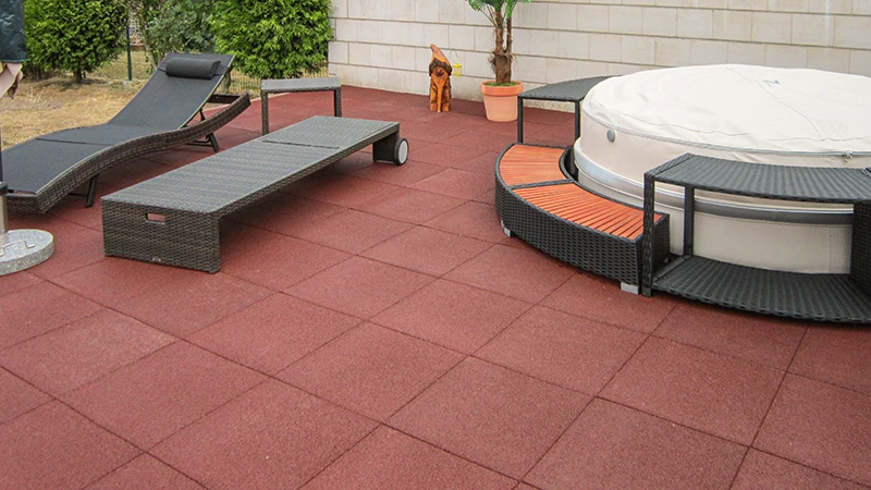 Un amplio espacio al aire libre con baldosas rojas WARCO para terraza, fabricadas en granulado de caucho aglutinado con PU, que proporcionan una pisada cómoda y una gran resistencia. Está equipado con muebles de jardín acogedores y un jacuzzi que se integra perfectamente en el conjunto. La superficie elástica amortigua los pasos, resiste las inclemencias del tiempo y requiere poco mantenimiento. Gracias a su acabado antideslizante, ofrece una solución atractiva para relajarse con estilo en exteriores. Ideal para terrazas modernas que buscan funcionalidad y confort.